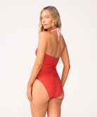 A woman wearing a red one piece swim suit standing against a white wall.