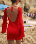 Back shot of a woman wearing a long sleeve mini dress walking on a beach.