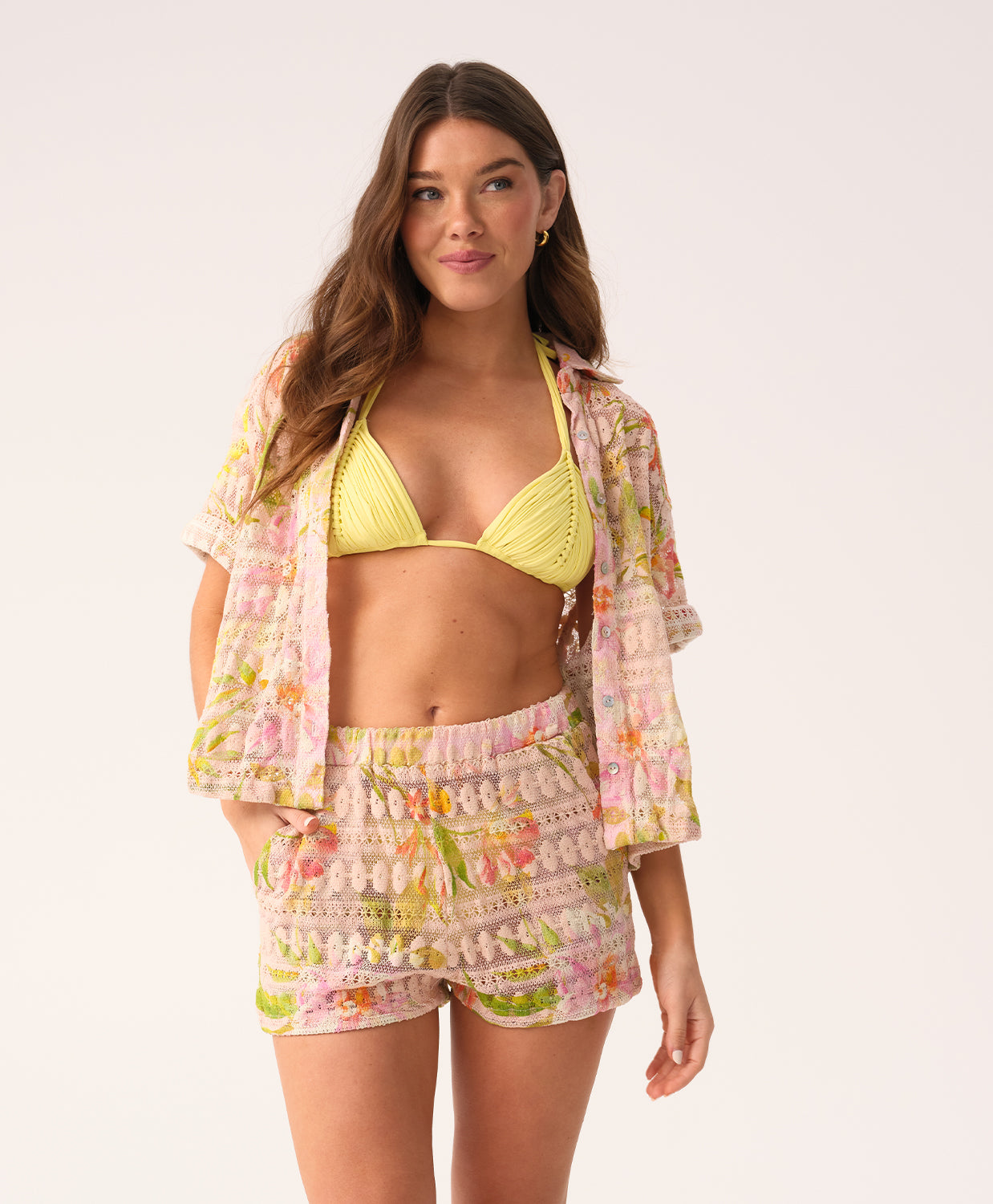 Woman wearing a yellow bikini with a floral cover-up on a white background