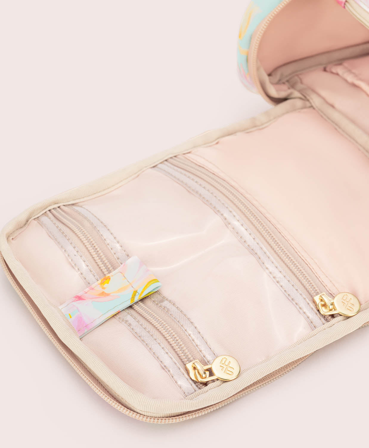 Beige toiletry bag with floral accents on a light pink background