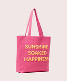 Pink tote bag with 'Sunshine Soaked Happiness' text on a light pink background
