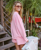Woman in a pink outfit standing next to a suitcase with plants in the background