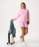 Woman in pink outfit holding a denim jacket and white suitcase on a white background