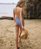 A woman wearing a blue and white striped one piece swim suit walking on a beach near the ocean.