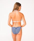 A woman wearing a blue and white striped bikini facing towards a white wall.
