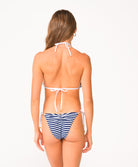 A woman wearing a blue and white striped bikini facing towards a white wall.