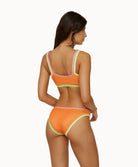 Back view of woman wearing a orange crochet bikini in front of a white background. 