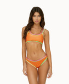 Woman wearing a orange crochet bikini in front of a white background. 