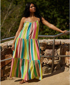 A woman wearing a floor length multi colored dress standing outside leaning against a metal railing.