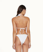 Back view of brunette woman wearing a white bikini in front of a white background. 