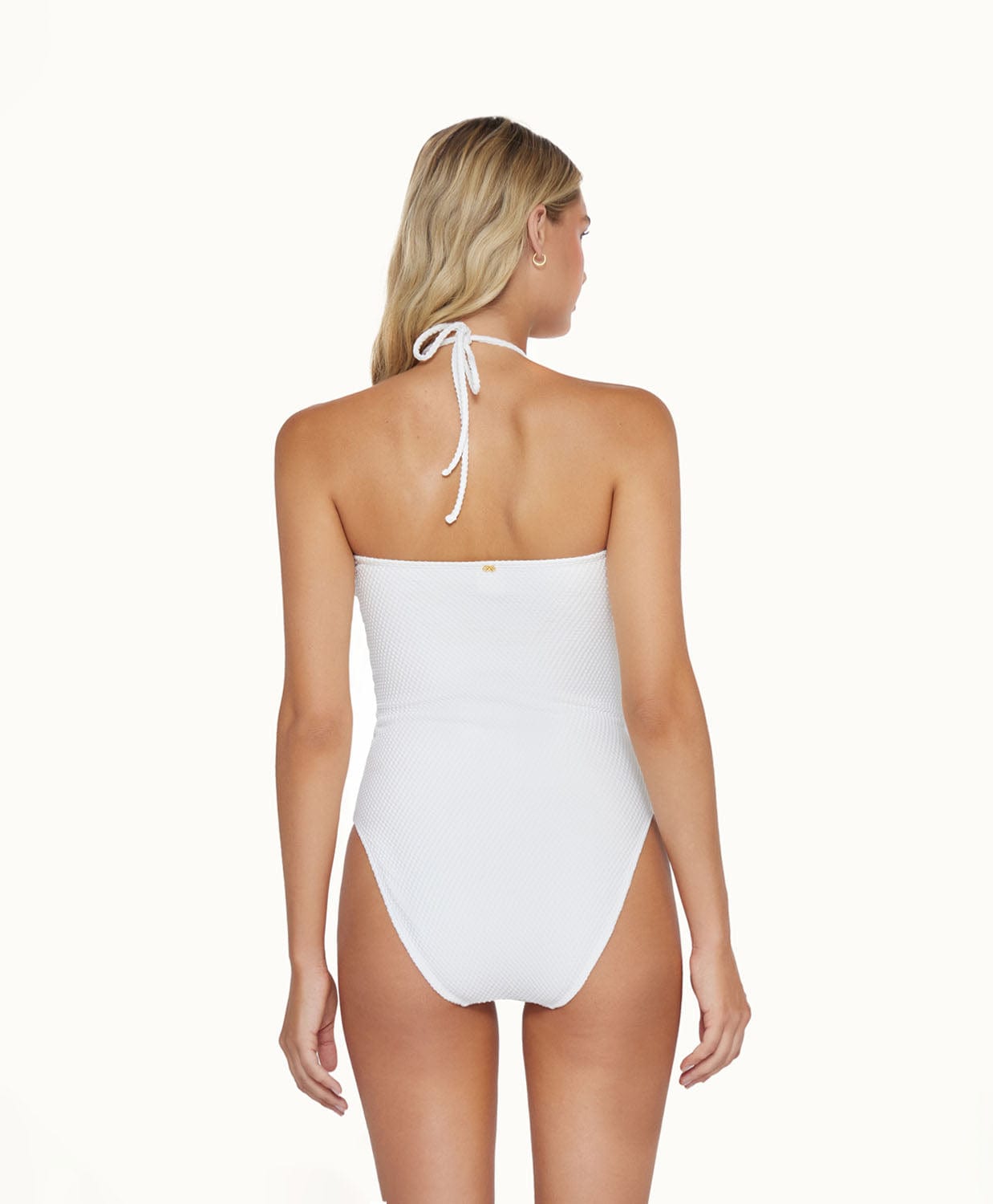 Back view of blonde woman wearing a white one piece in front of a white background. 