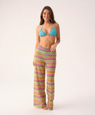 Woman wearing a blue bikini top and colorful striped pants on a white background