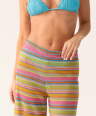 Woman wearing a blue triangle bikini top swimsuit and striped pants with a plain background