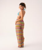 Woman wearing a blue bikini top and colorful striped pants on a white background