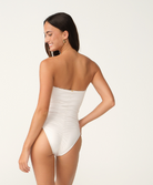 A woman modeling a strapless white high-cut one-piece swimsuit, shown from the back against a plain off-white studio background.