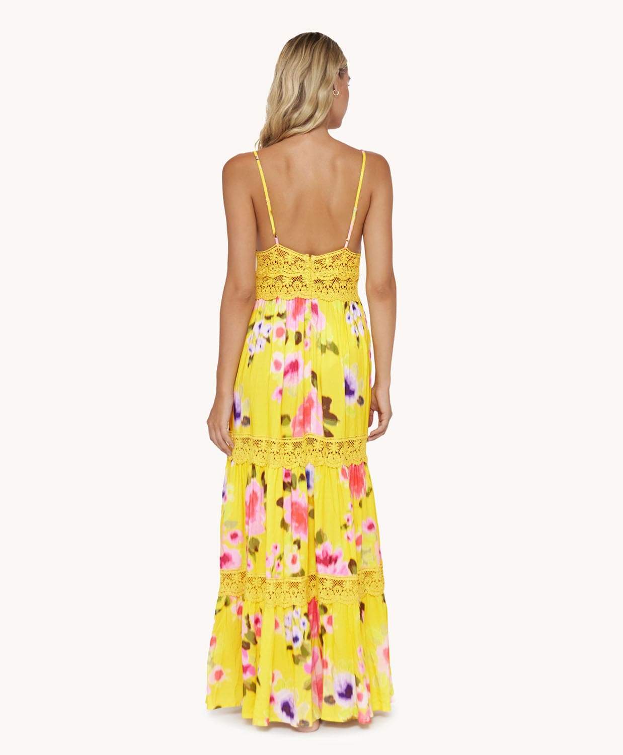 Back view of blonde woman wearing a yellow long dress in front of a white background. 