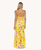 Back view of blonde woman wearing a yellow long dress in front of a white background. 