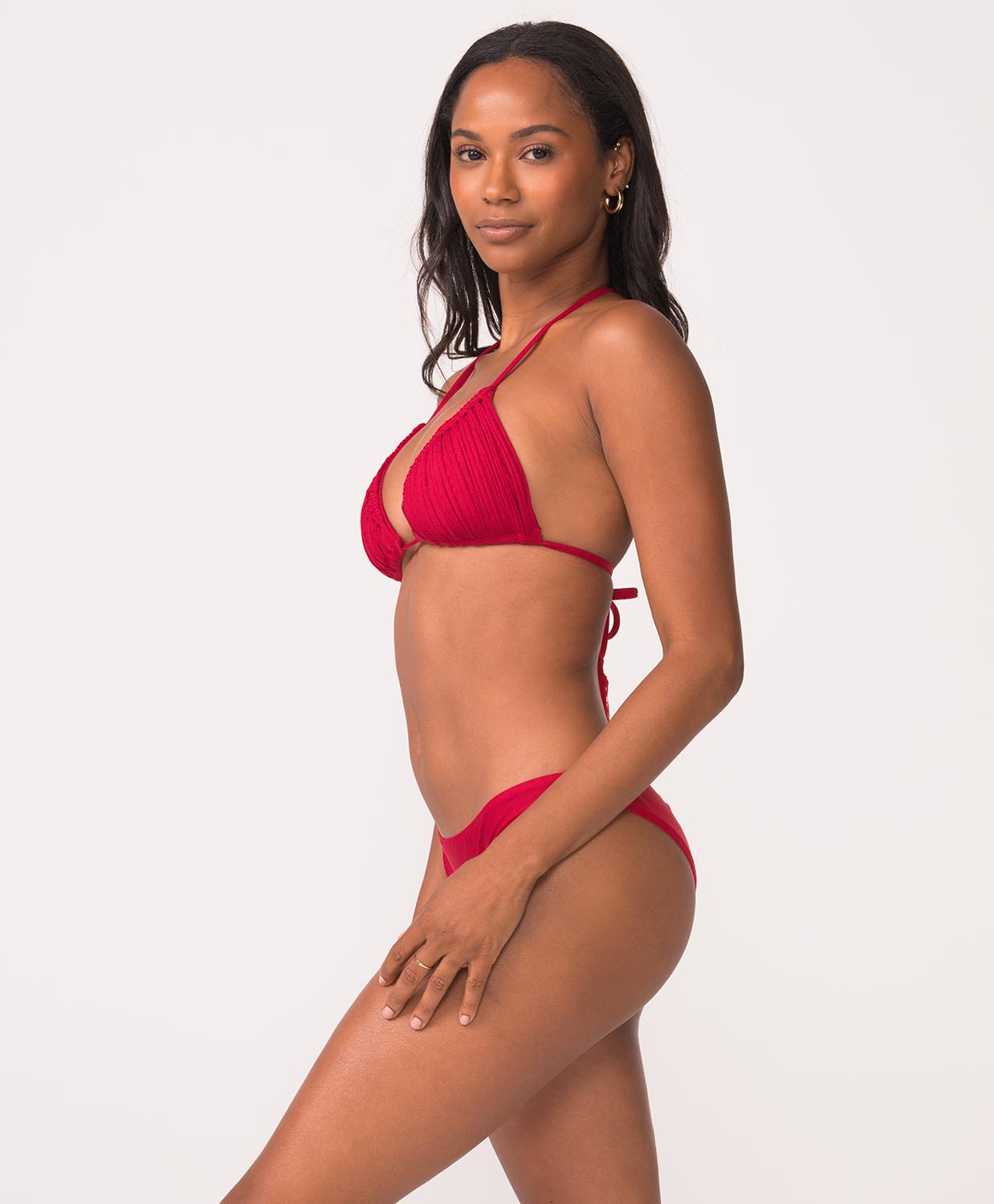 Woman wearing a red bikini with macrame detailing stands in front of white wall.