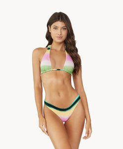 Brunette woman wearing a multi-colored stripe print halter bikini stands in front of white wall.