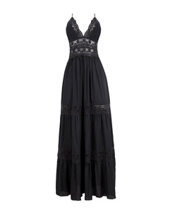 A black full length dress with embroidery details. Featured against a white wall background.