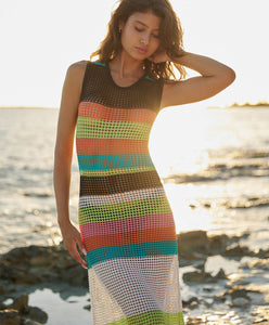 Brunette woman wearing a multi-colored striped full length dress stands on the beach.
