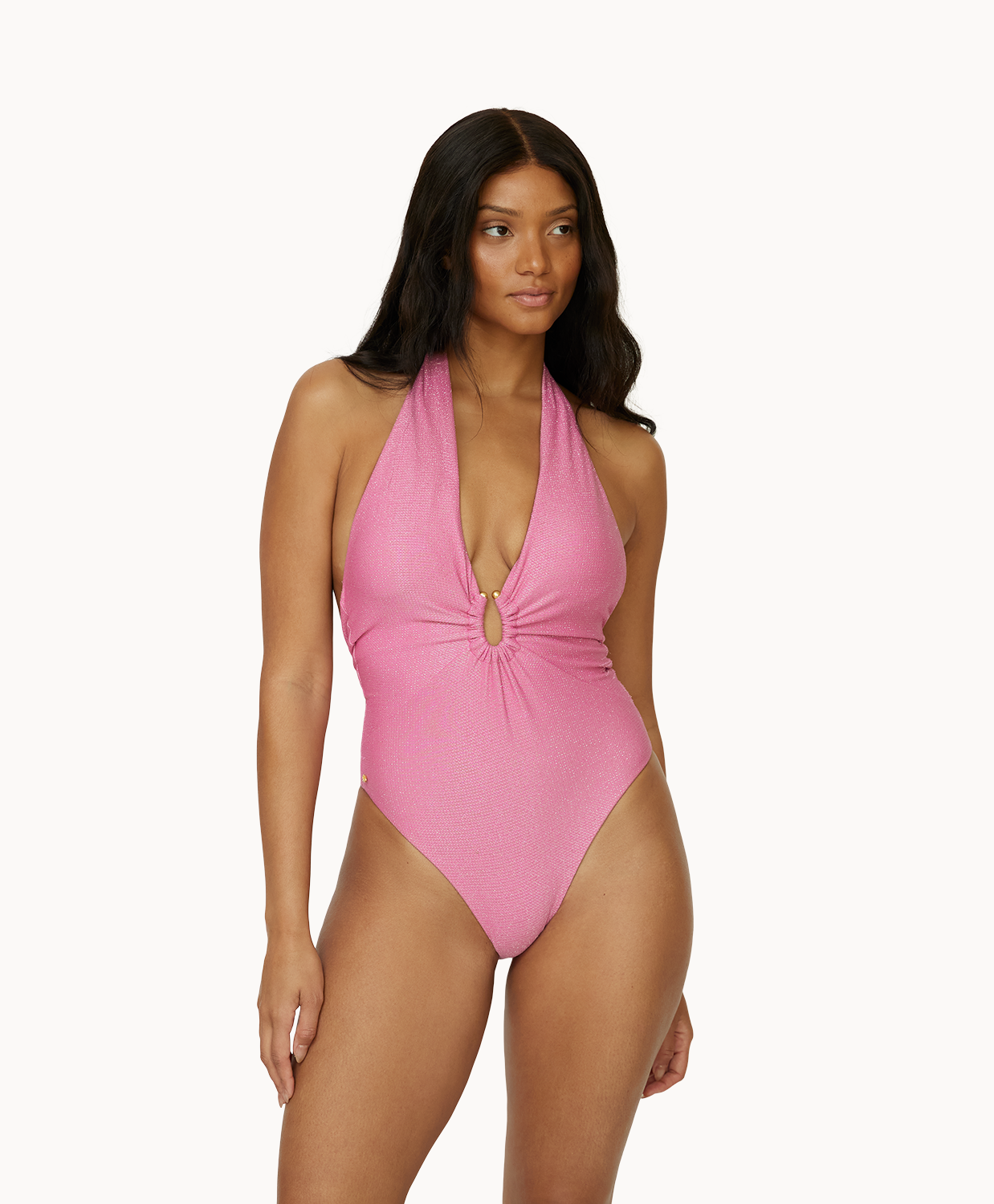 A woman wearing a pink one piece swimsuit standing against a white wall. 