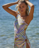 A blonde woman wearing a multi colored dress standing near the water. 