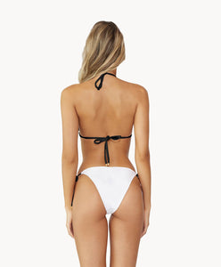 Blonde woman wearing a black and white triangle bikini with stud details facing backwards towards white wall.