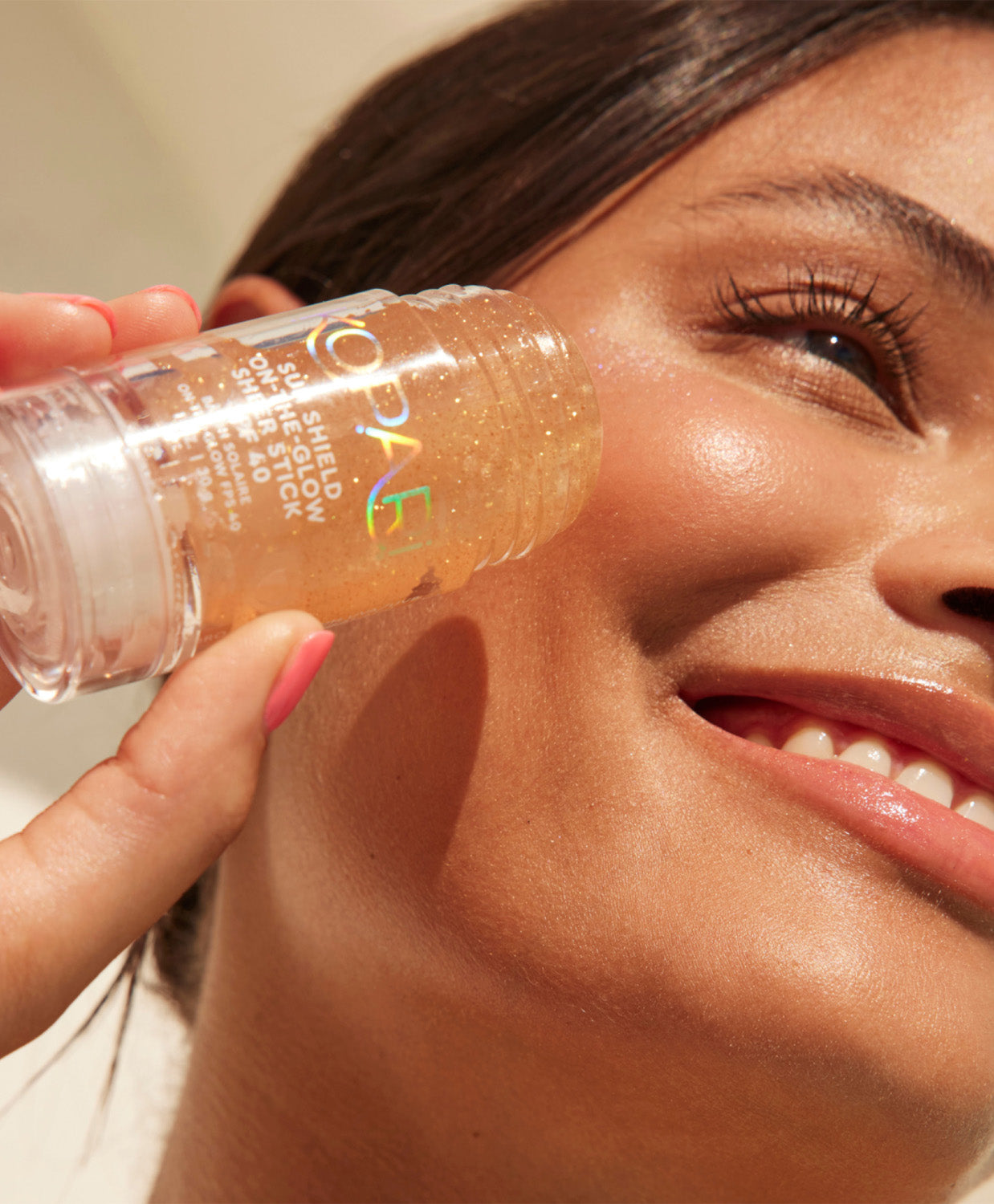 A smiling woman applying the Kopari Sun Shield stick to her cheek in direct sunlight.