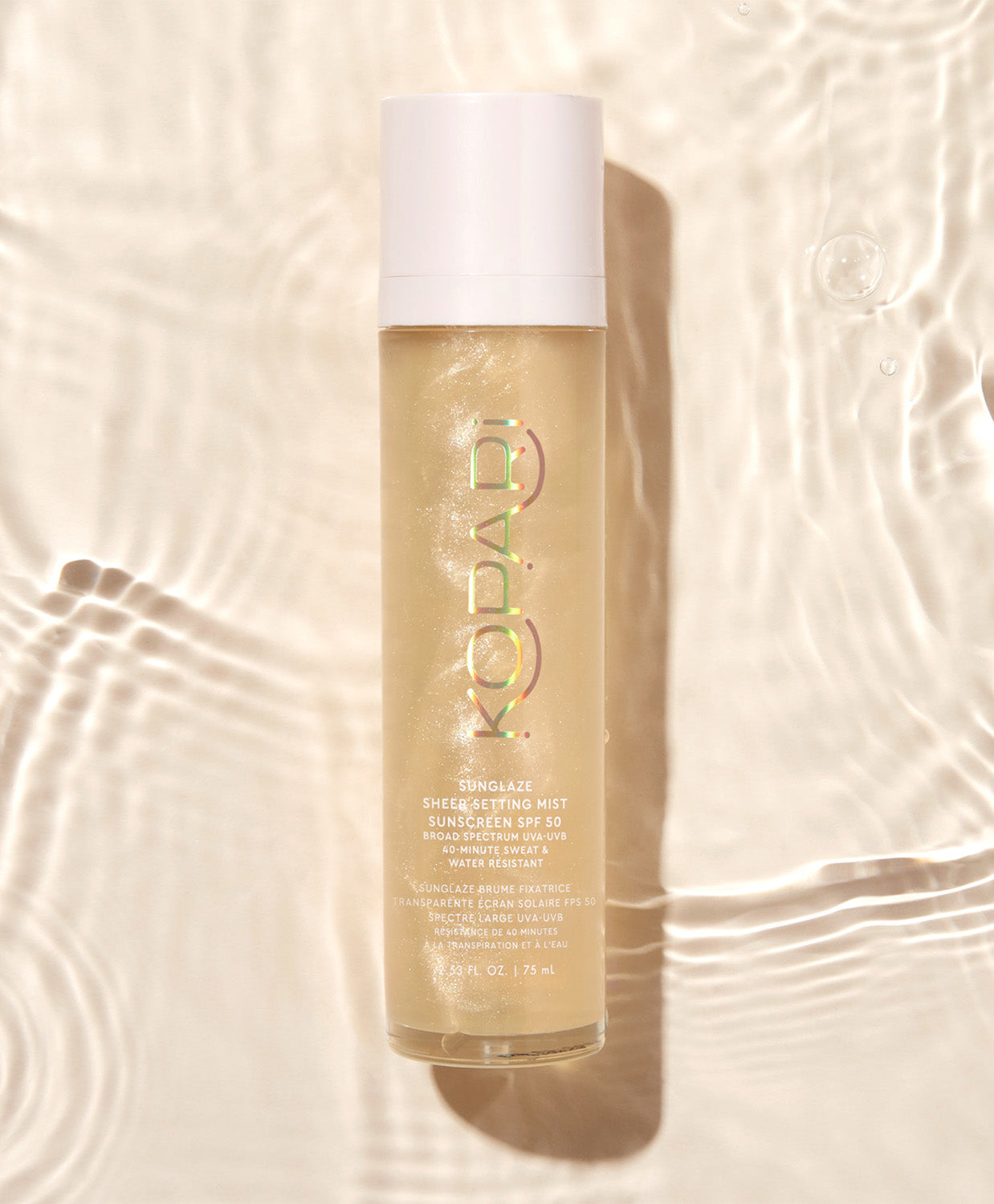 The Kopari Sun Shield spray bottle floating in water with ripples and sunlight reflecting off the surface.