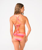 A woman wearing a red, pink, and orange shimmery ombre bikini set facing away in front of a white background.