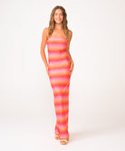 A woman wearing a long red, pink, and orange strapless ombre tube dress in front of a white background.