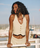 A woman wearing a tan sleeveless top and matching tan pants leaning against a white dock.