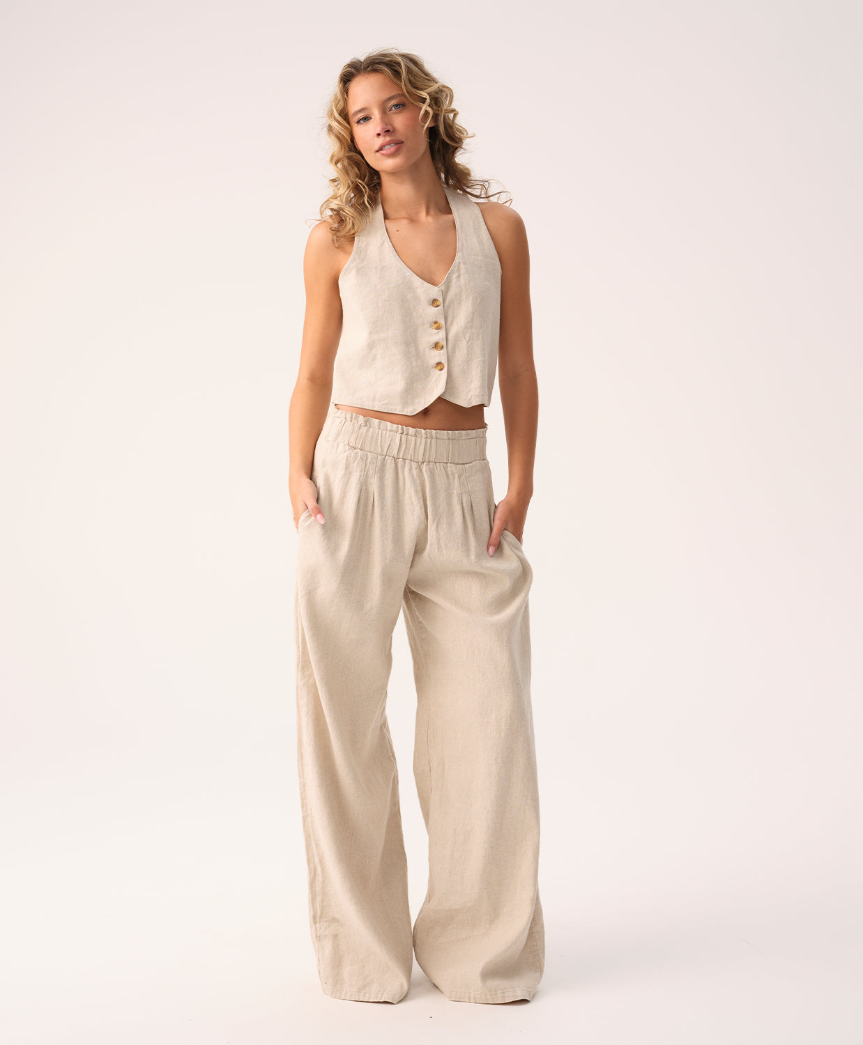 Woman wearing a beige sleeveless top and wide-leg pants on a white background