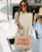 Woman holding a woven bag with 'MORE AMORE' text on a boat