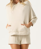 Person wearing a beige hoodie and shorts set on a white background