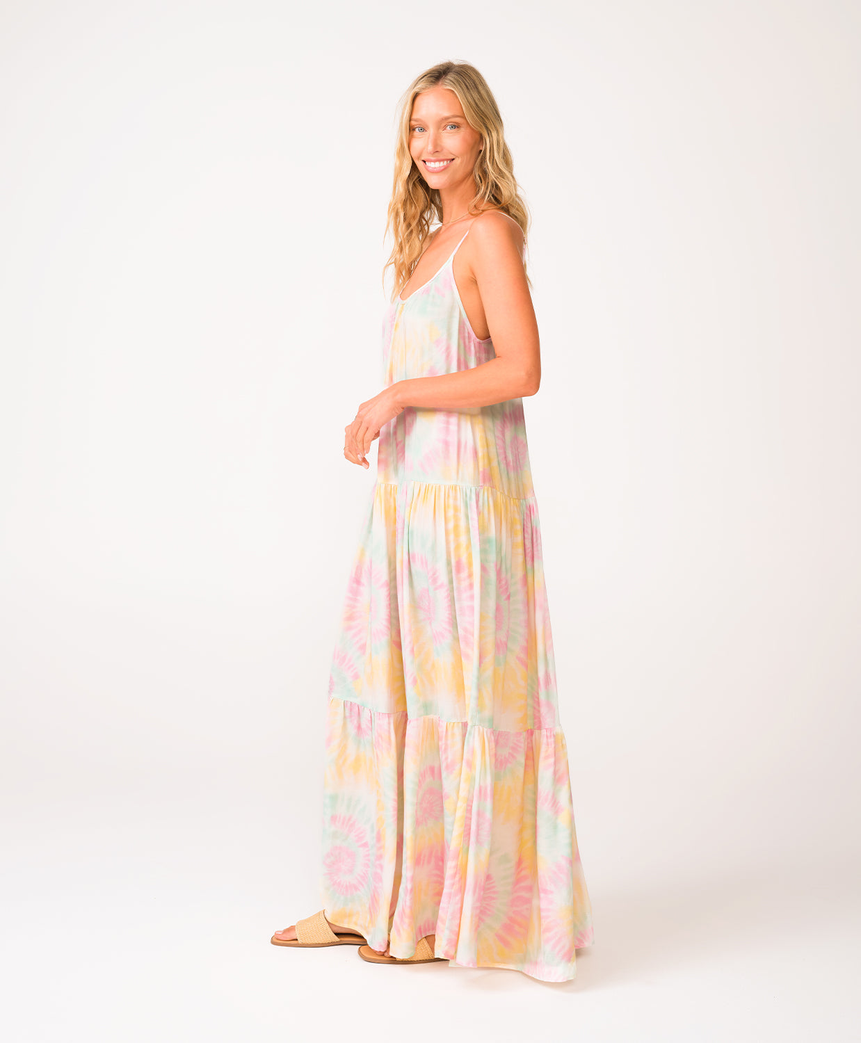 A woman wearing a tie dye long dress standing in front of a white wall.
