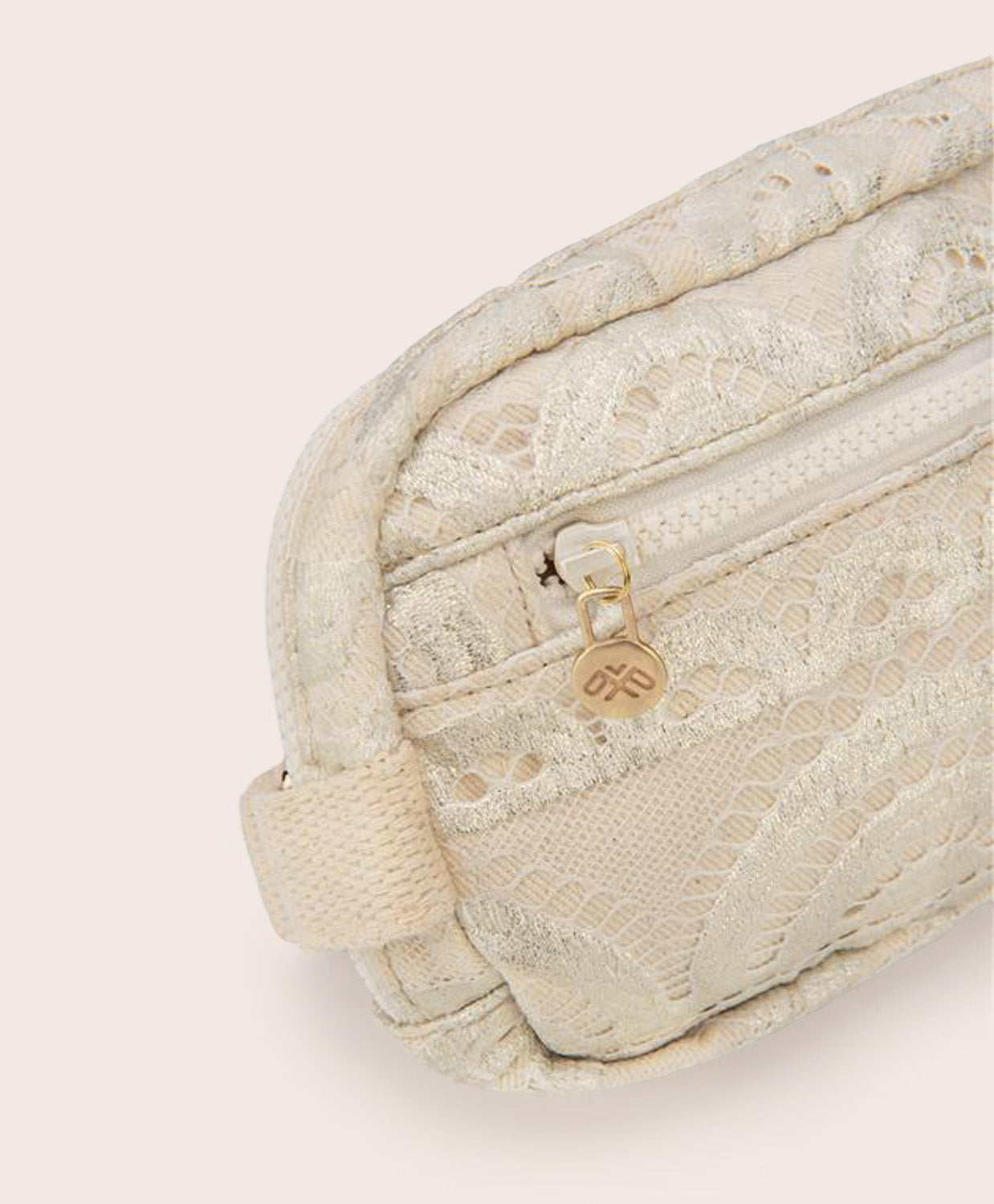 A tan colored lace crossbody bag against a white wall.