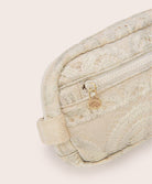 A tan colored lace crossbody bag against a white wall.