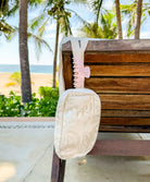 A cream colored lace crossbody purse and a pink hair clip hanging on a bench outside.