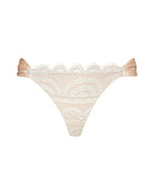 A tan and cream lace bikini against a white wall.