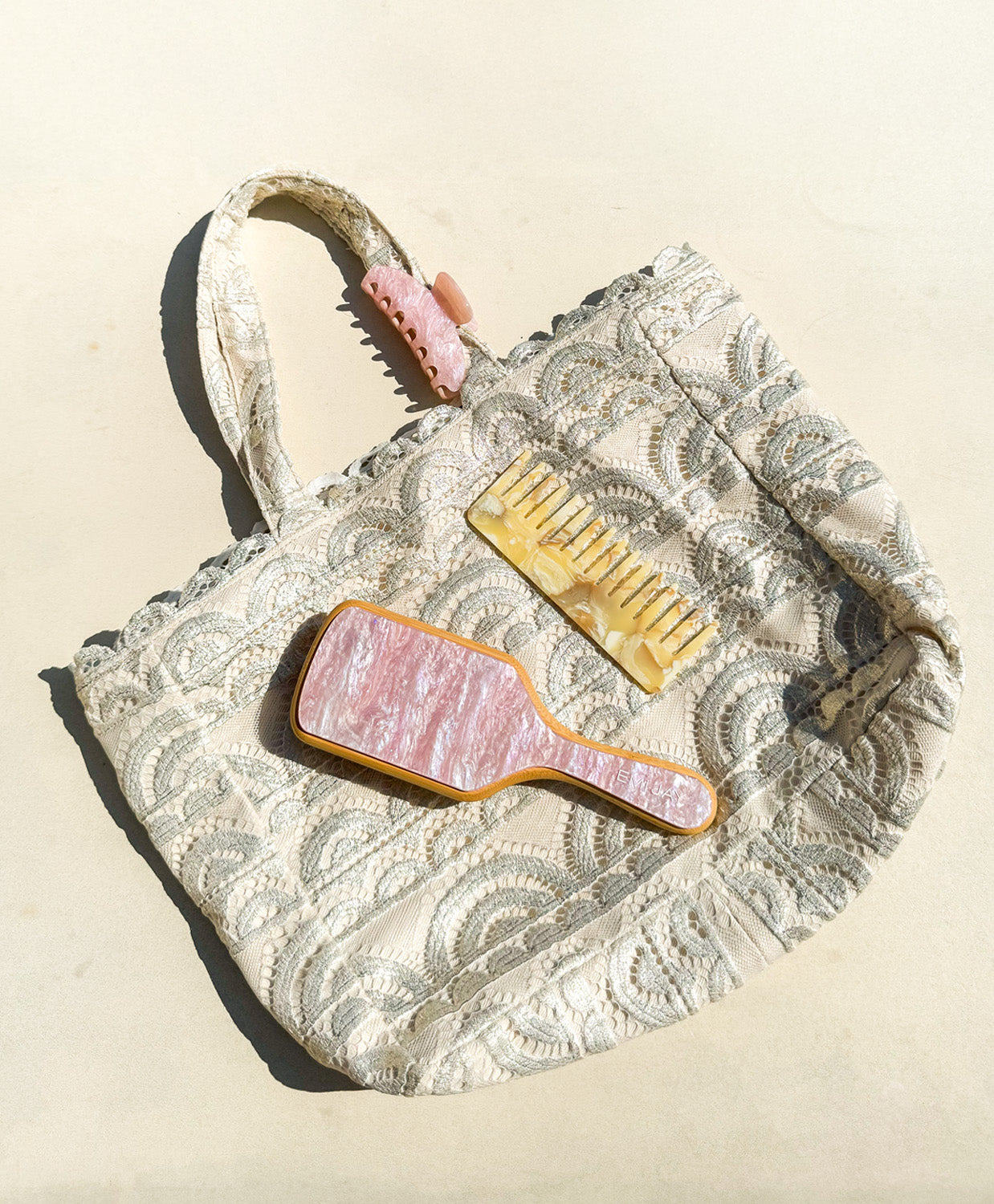 A tan lace tote with a brush, comb, and clip laying on white ground. 