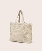 A tan lace tote with scalloped trim against a white wall. 