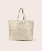 A tan lace tote with scalloped trim against a white wall. 