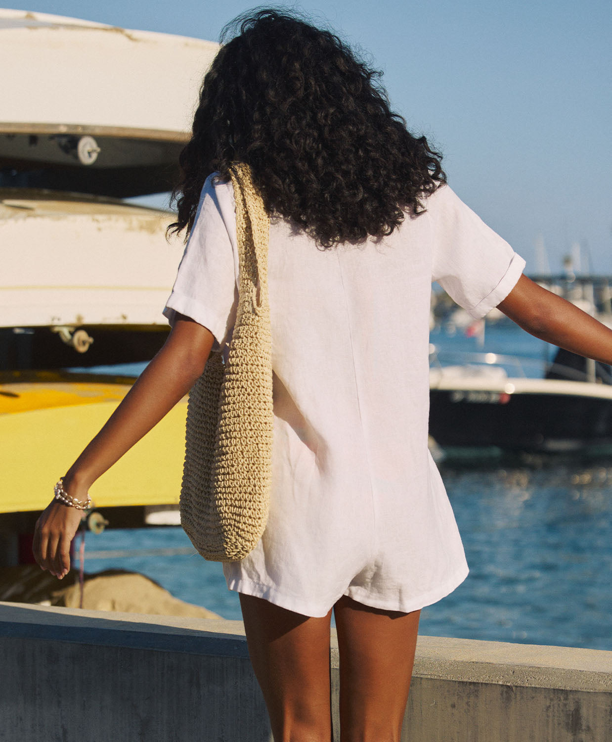 Woman with a woven bag walking by boats on a dock