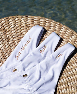Three white bikini bottoms with gold embroidering laying flat on a wicker basket near the water.  