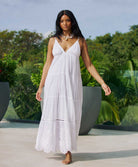 A woman wearing a long white dress withe embroidery details standing outside near plants.