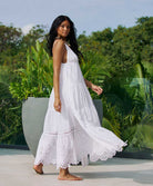 A woman wearing a long white dress standing outside near plants.