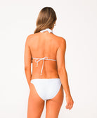 A woman wearing a white lace halter bikini standing against a white wall.