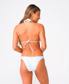 A woman wearing a white lace halter bikini standing against a white wall.